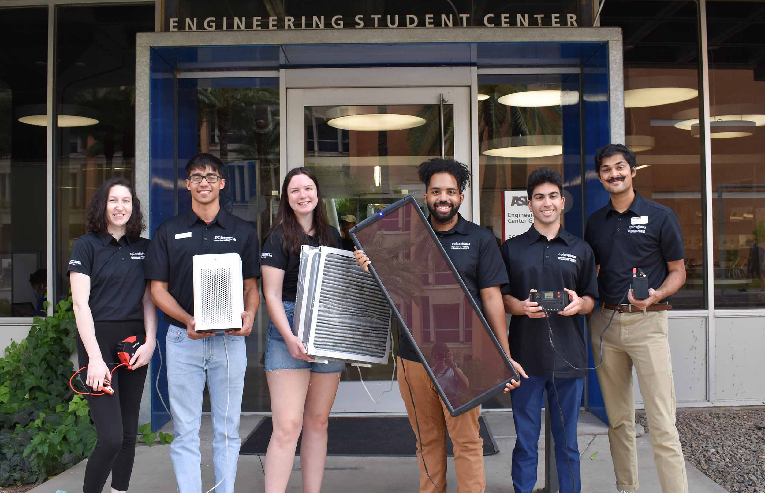Six EPICS team members from Project Koyash pose for a group shot in front of the Engineering Student CEnter holding objects related to their projects
